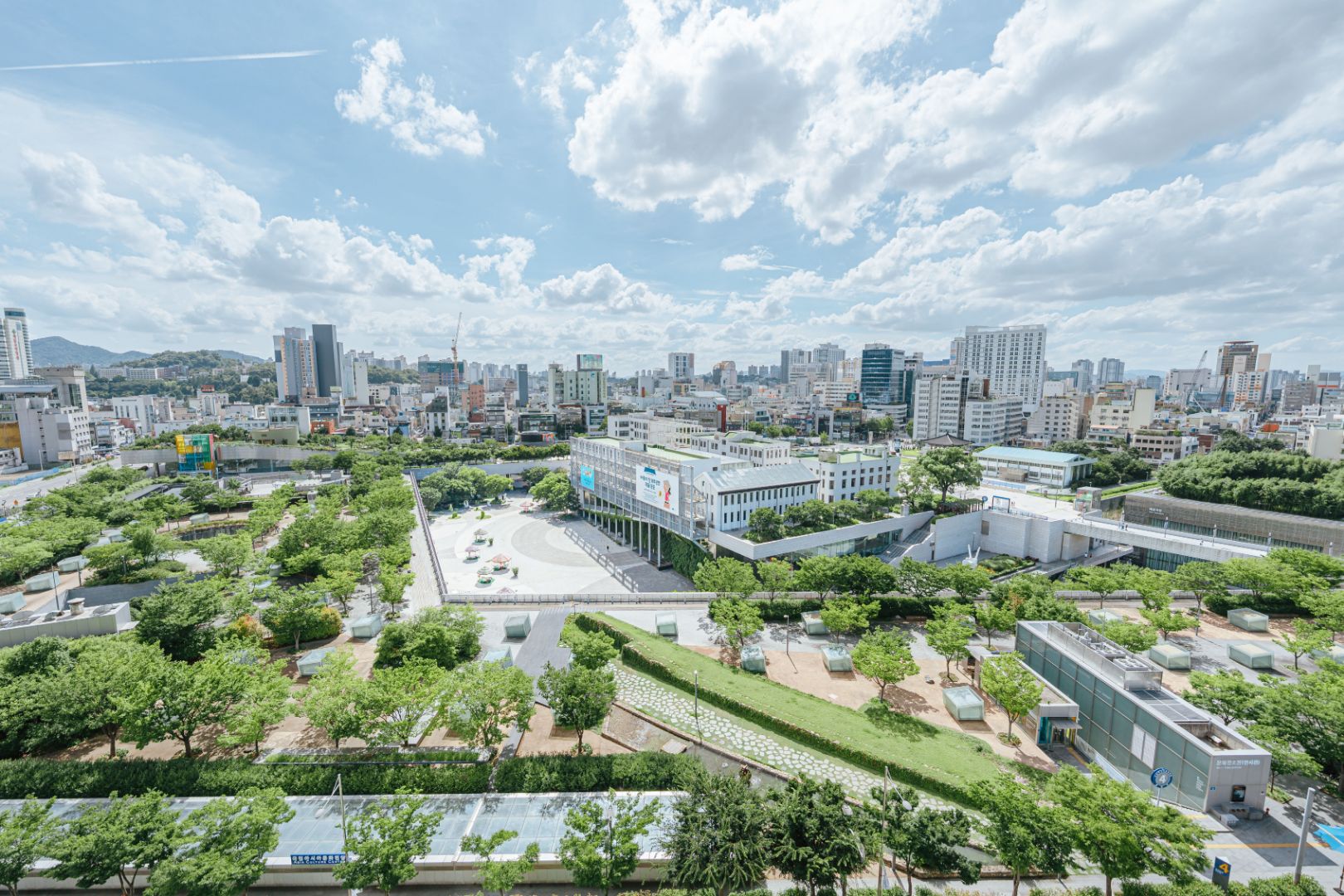 Pemandangan kampus KAIST dengan gedung modern, area hijau yang luas, dan latar belakang kota dengan langit cerah berawan.